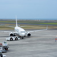 駐機場を離れプッシュバックされる飛行機と誘導するグランドハンドラー（山口宇部空港）の写真