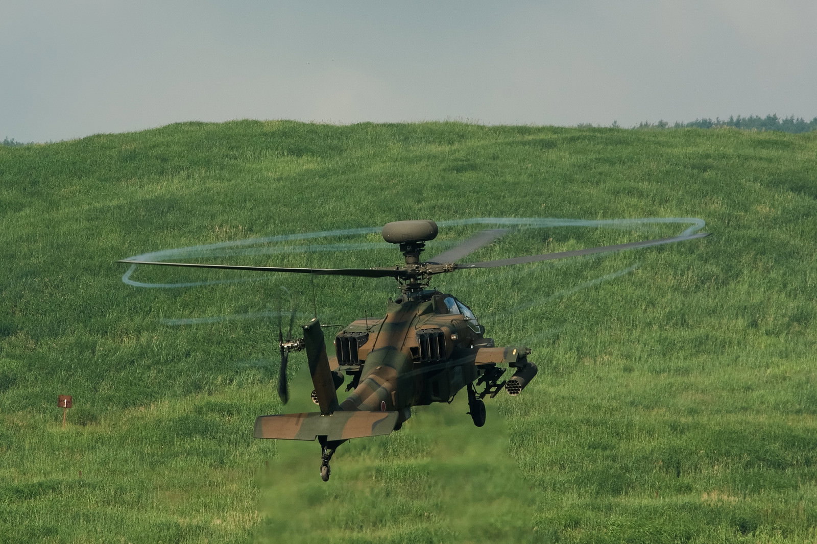 富士総合火力演習で緑の草原上空を飛行するアパッチ攻撃ヘリコプター