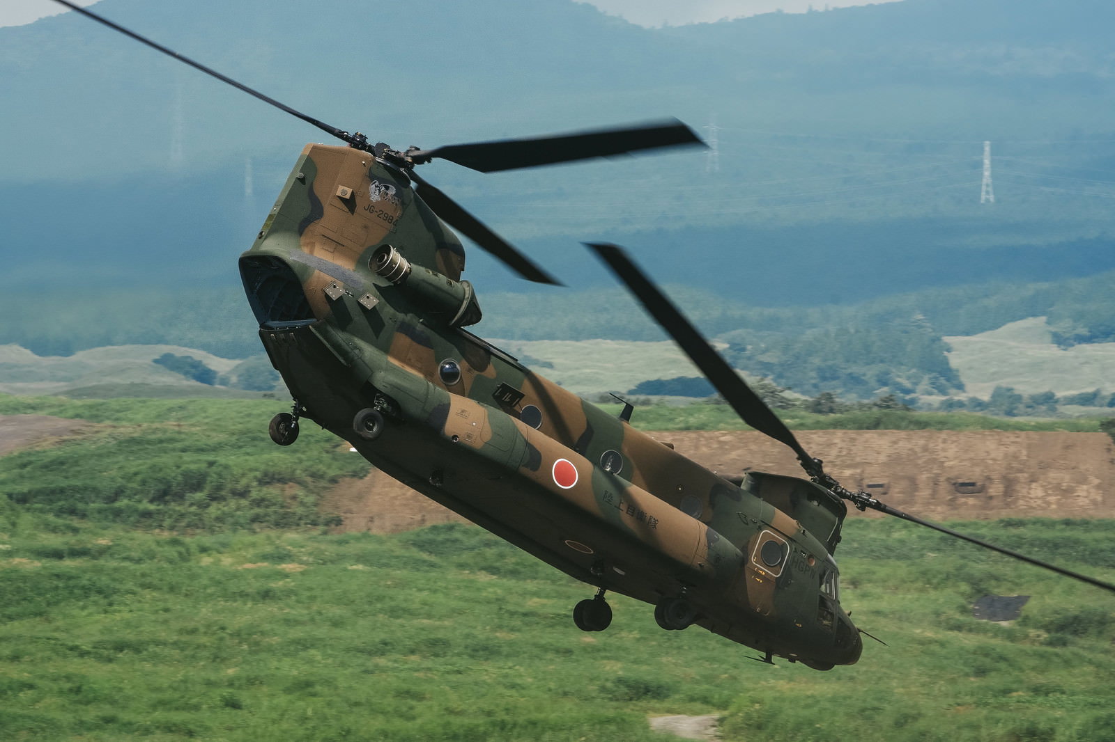 草原上空を飛行する迷彩色のCH-47チヌーク輸送ヘリコプター