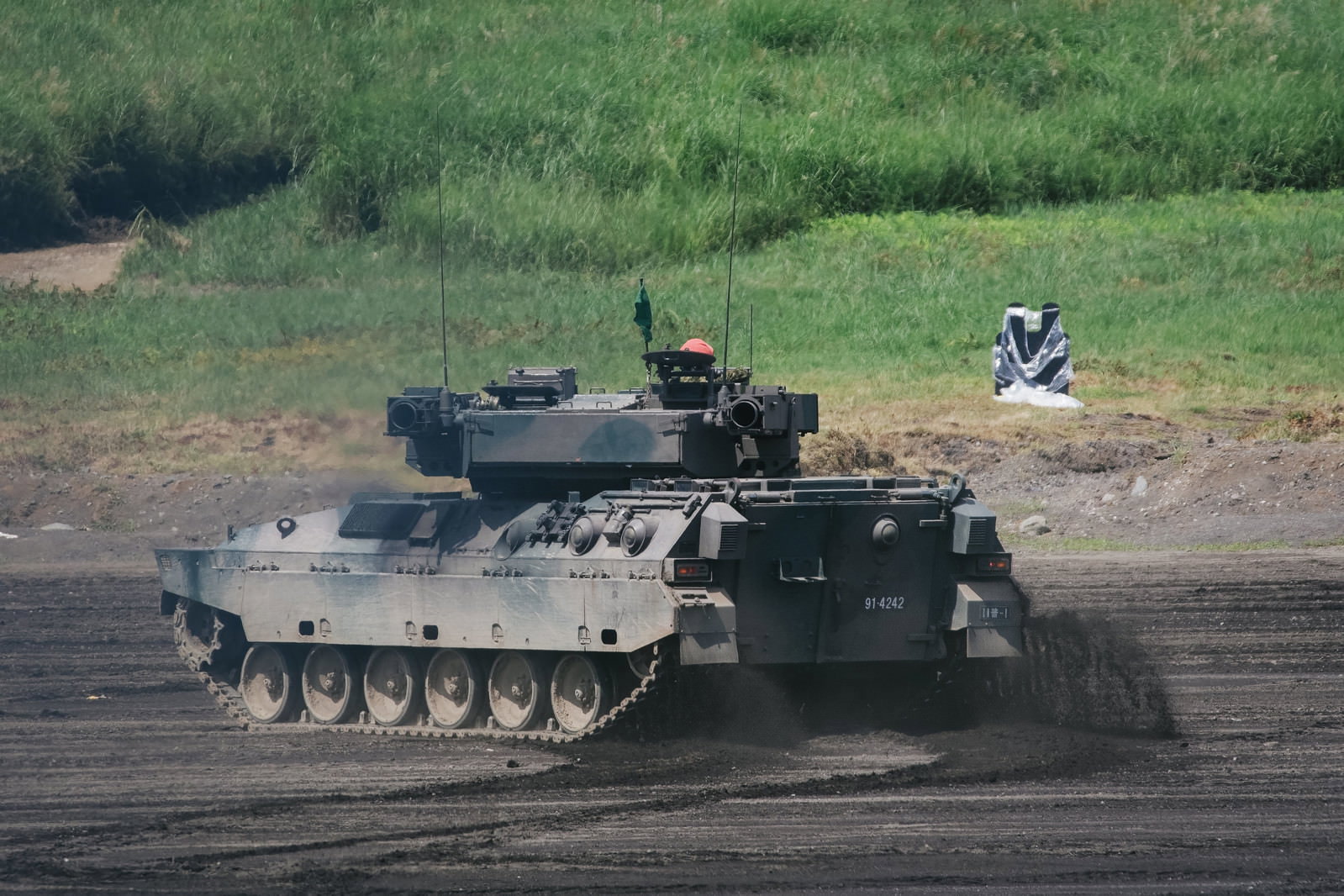 泥を蹴散らして進む89式装甲戦闘車と土煙が舞う演習場