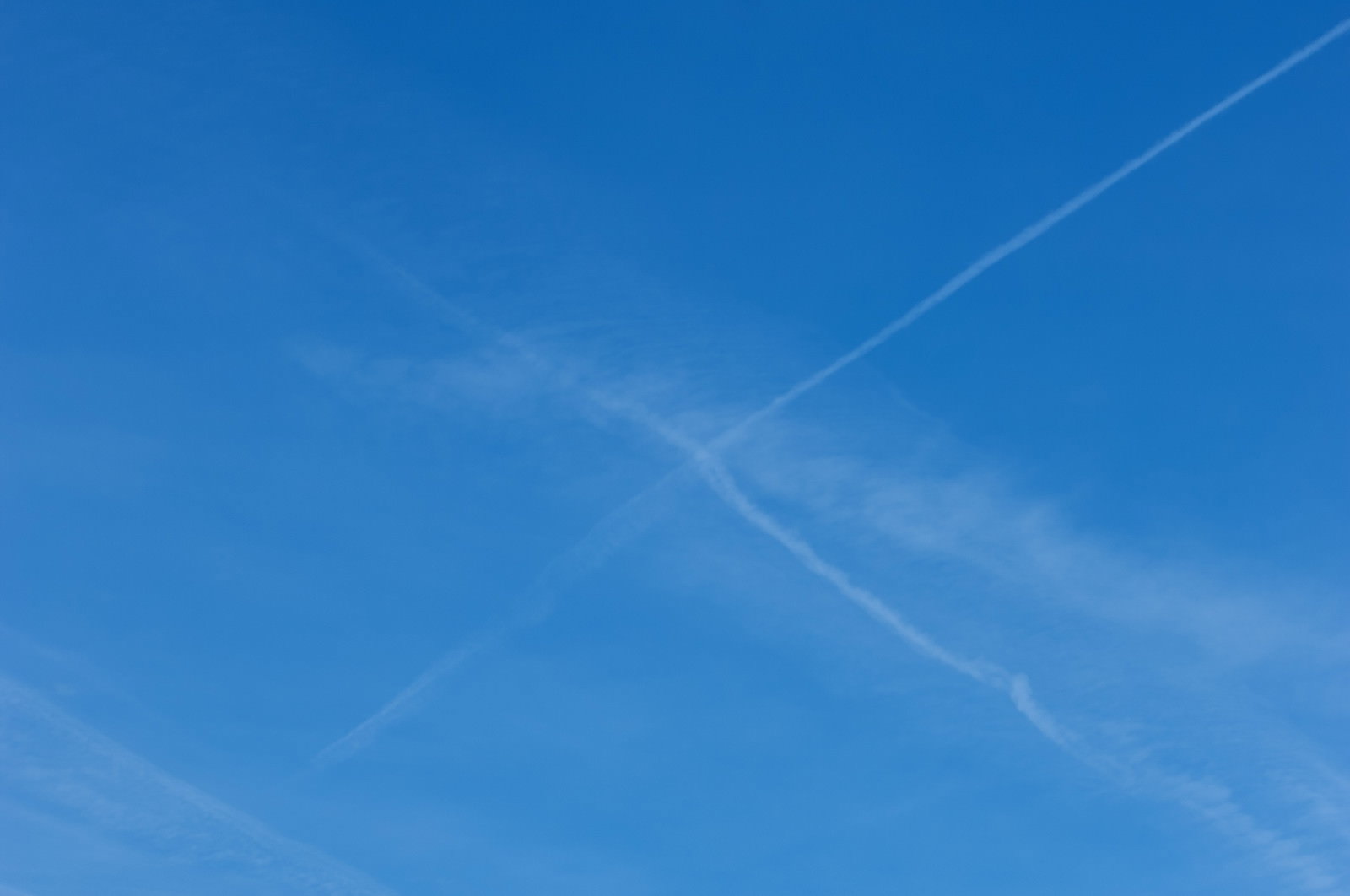 青空に飛行機雲が2本交差して薄れている