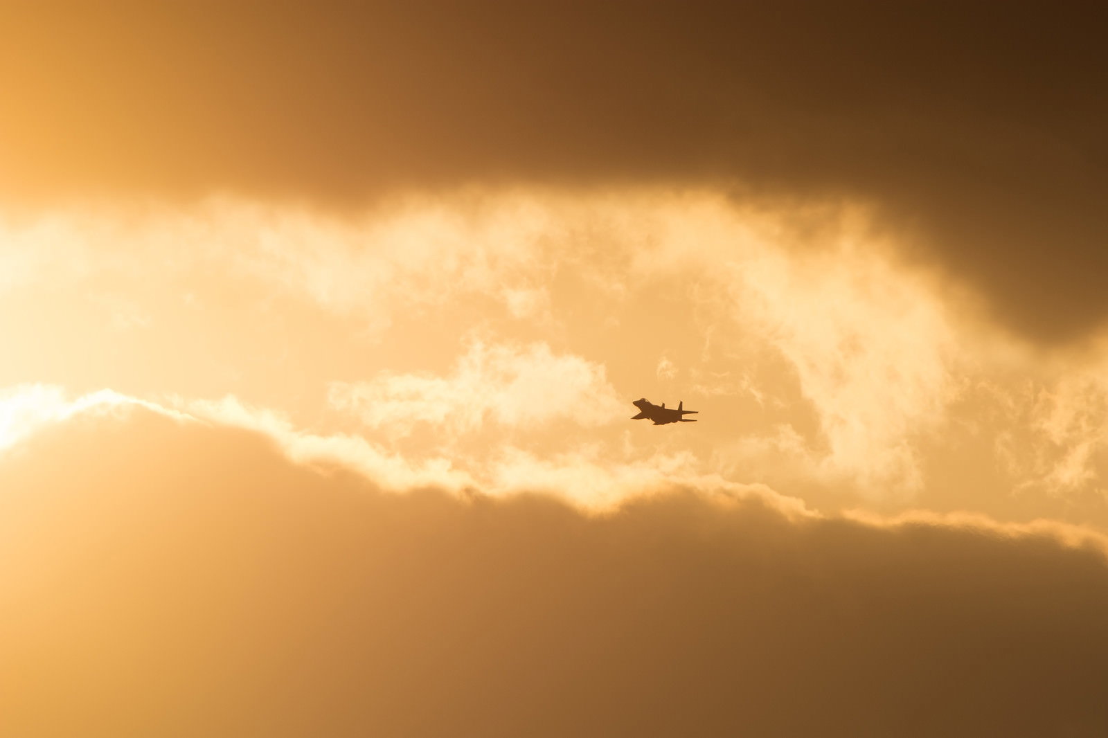 夕焼け雲から現れるF-15のシルエット