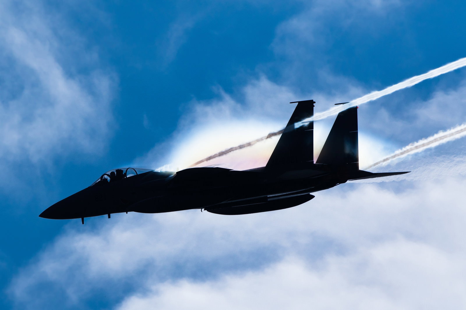 青空を背景に飛行するF-15戦闘機のシルエット