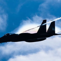 虹を纏って進む戦闘機のシルエット（F-15）の写真