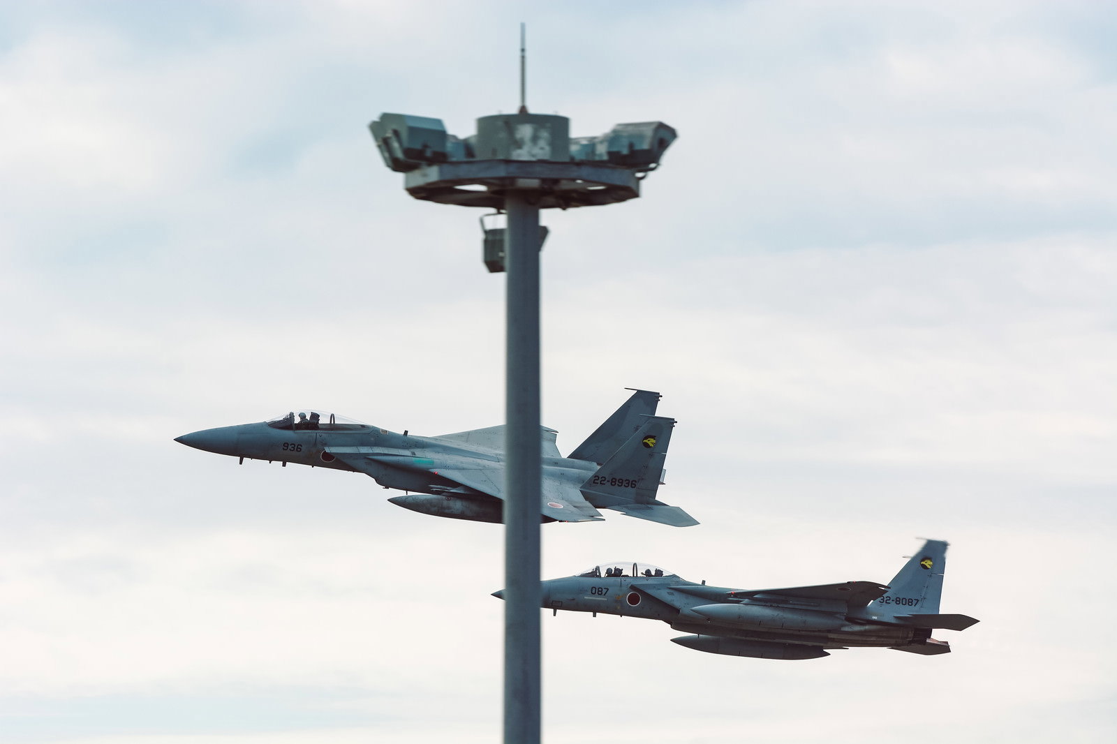 曇り空を背景に鉄塔の前を併走飛行する2機のF-15戦闘機