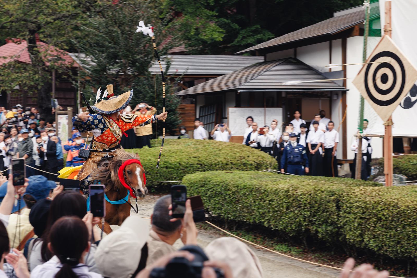 古殿八幡神社の境内で馬上から矢を放つ流鏑馬の射手と観客