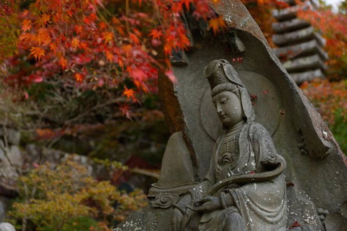 岩角寺の秋、紅葉に囲まれた石造の仏像と落ち葉