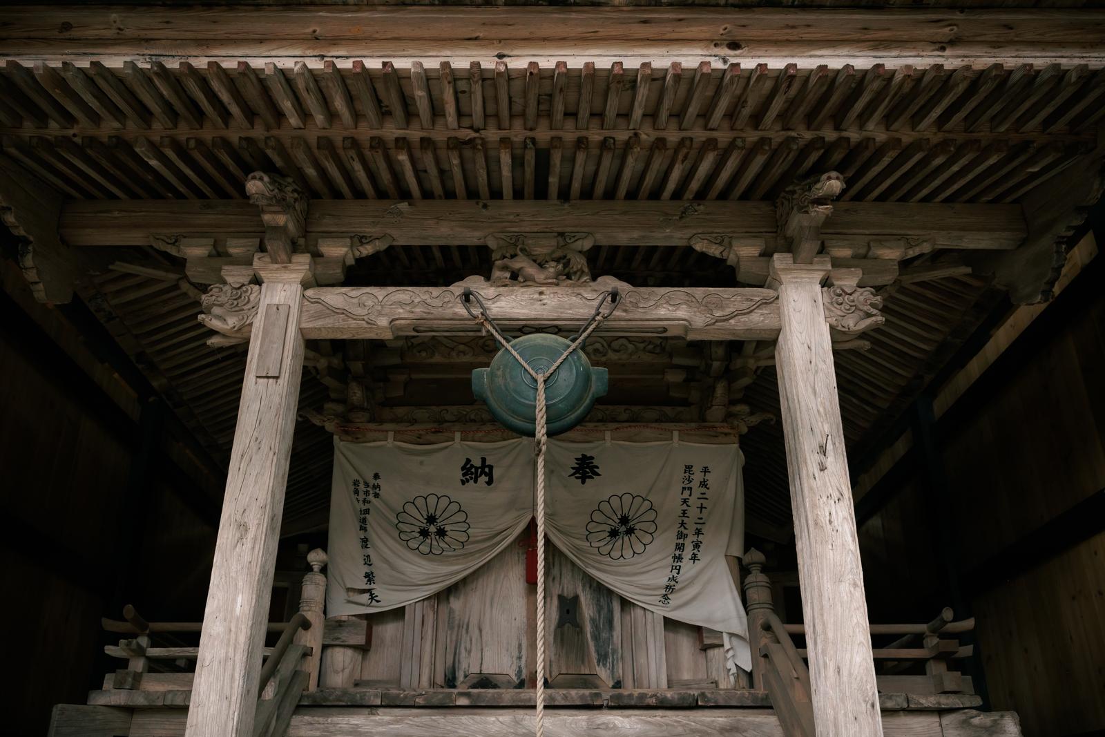 白い納奉幕が掛かった社殿の中央に吊るされた緑青色の鰐口