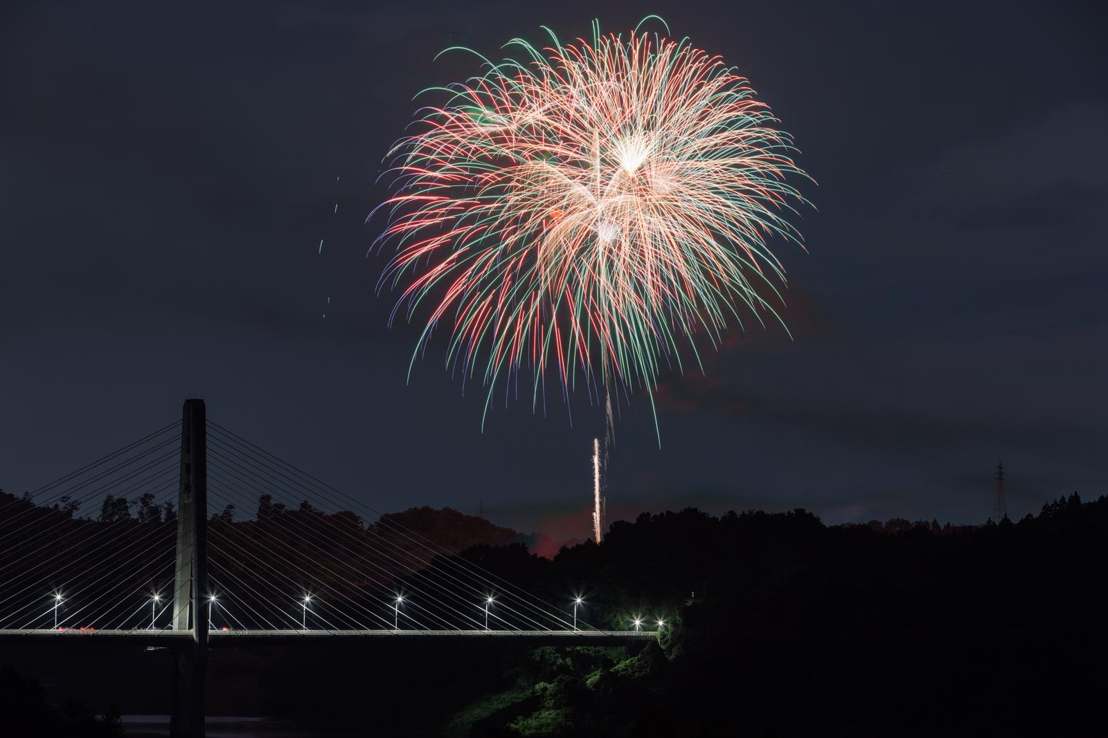 打ち上げ花火が咲く夜空と、ライトアップされた春田大橋のある夜景