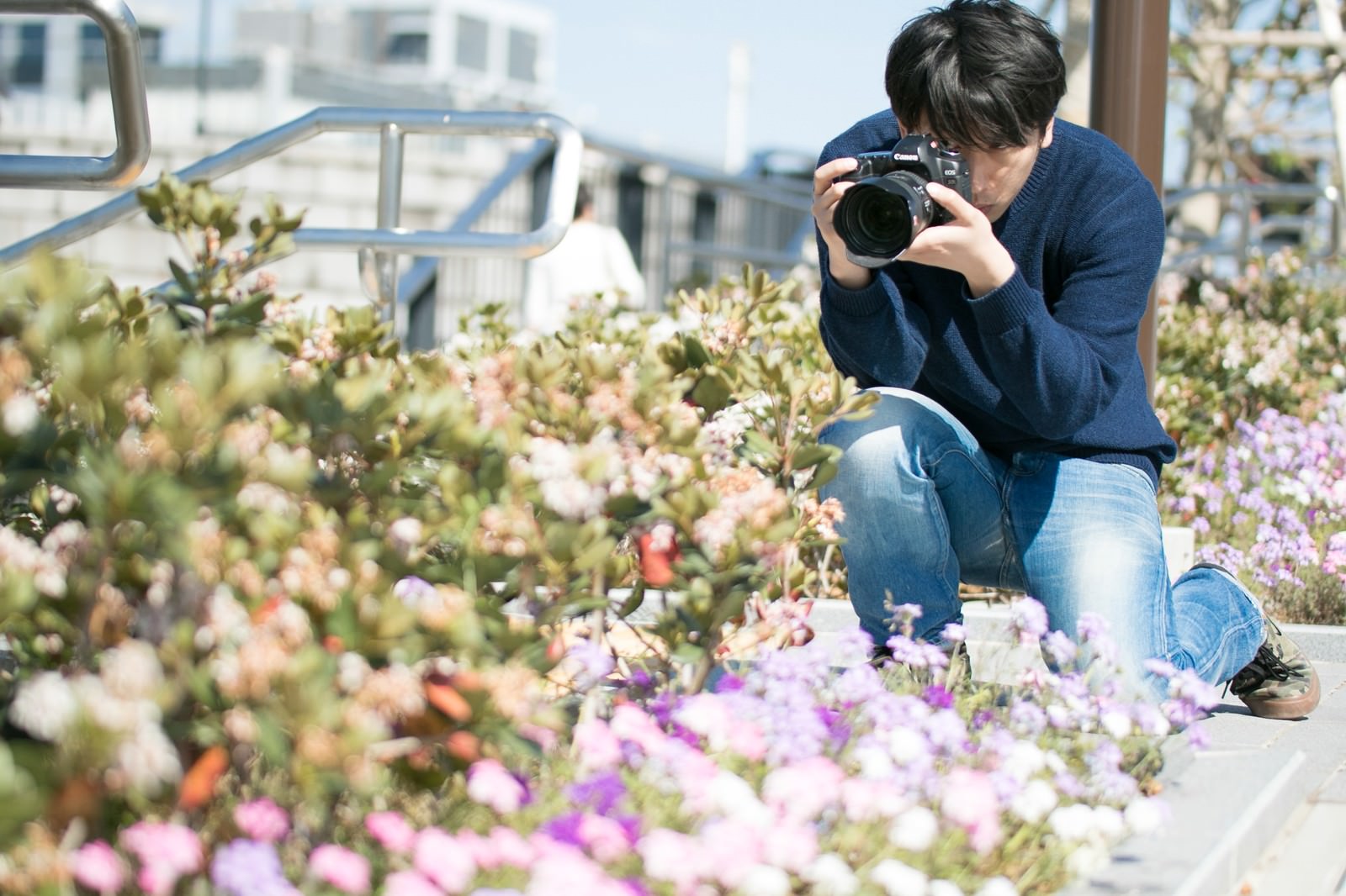 屋上の花壇で一眼レフカメラを構える男性フォトグラファー［モデル：大川竜弥］