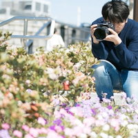 花壇で花を被写体にカメラを構える男性フォトグラファーの写真