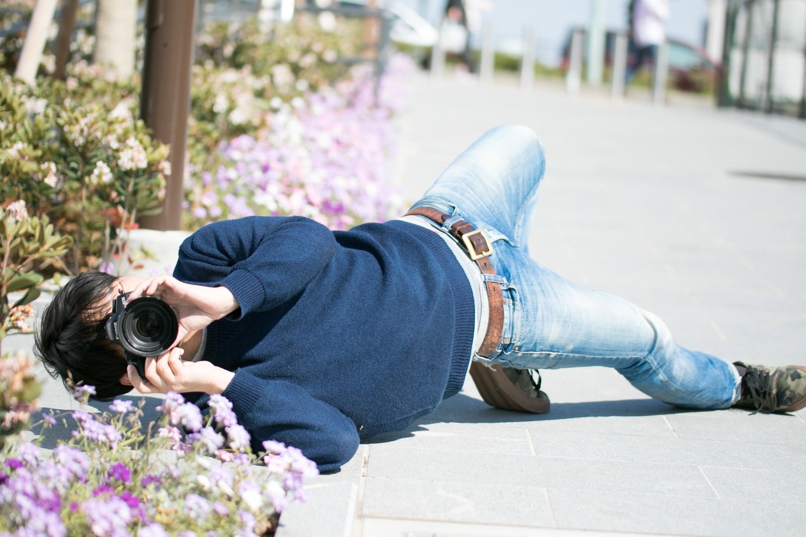 地面に寝転んでカメラを向ける男性カメラマン［モデル：大川竜弥］
