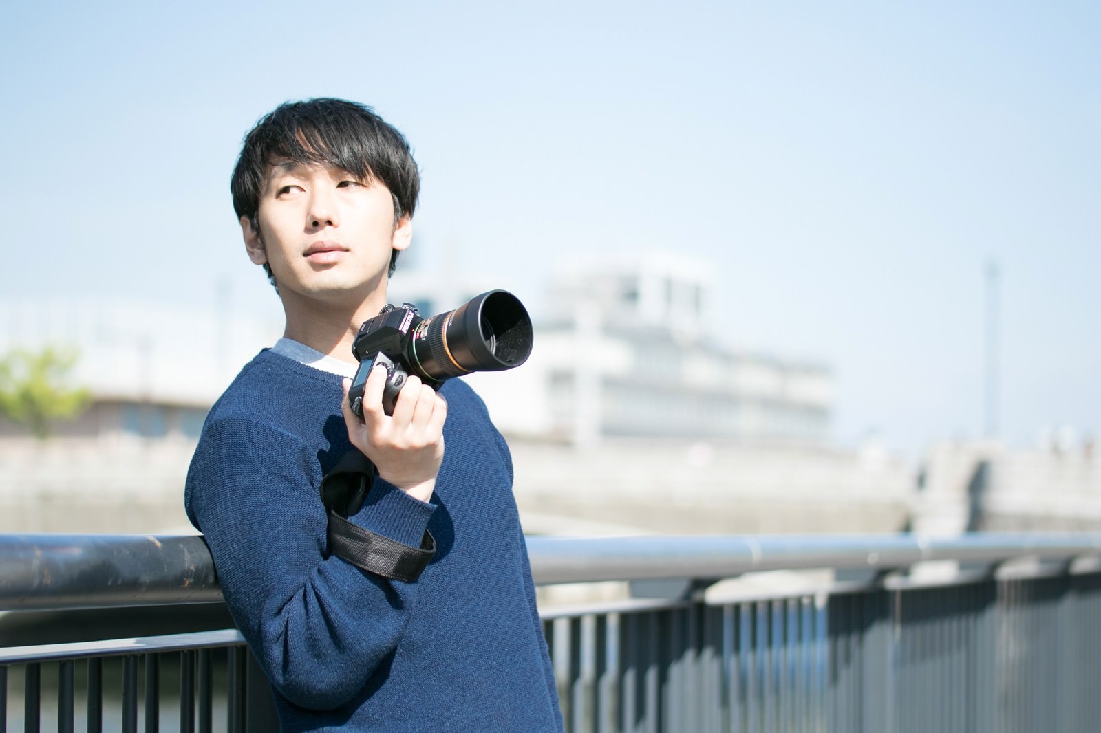 カメラを構えて空を見上げるフォトグラファーの男性［モデル：大川竜弥］