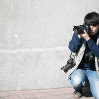肩にカメラをかける複数の撮影機材を持つカメラマンの写真