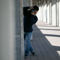 地味な作風を好む日陰男がコンクリート壁に身を隠してカメラを構えるの写真