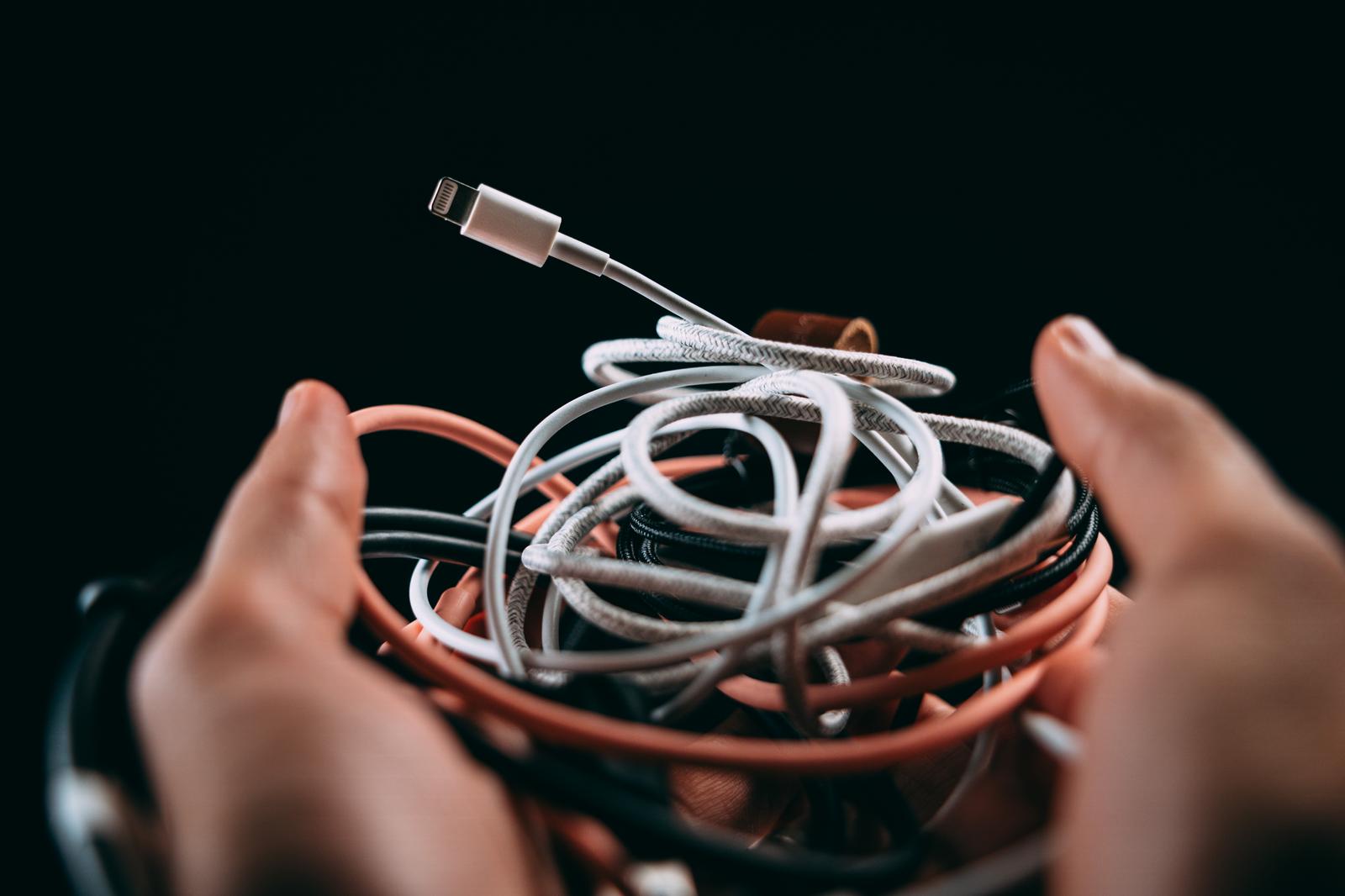 手に持った複数の絡み合ったLightningケーブルと充電ケーブル