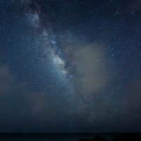 夜空に広がる天の川と岩礁が連なる静寂な海辺の写真