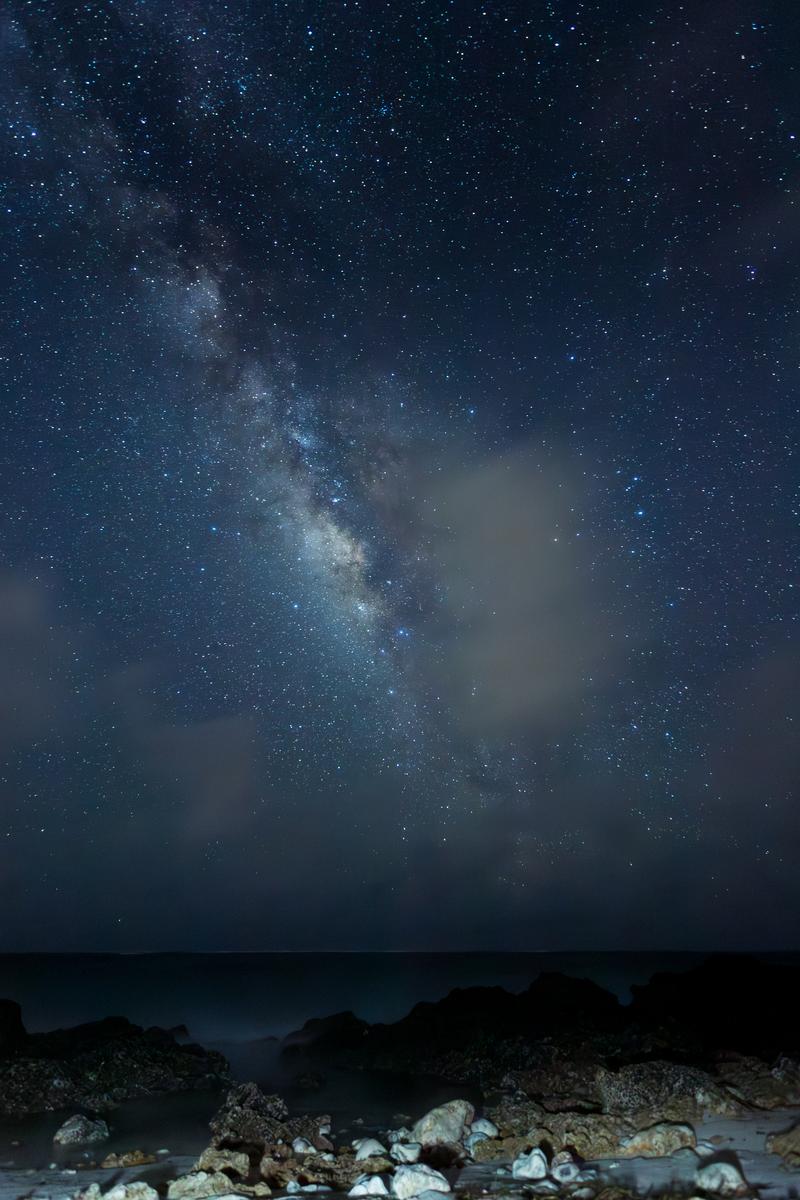満天の星と天の川が見える夜空の下、岩礁が連なる海岸