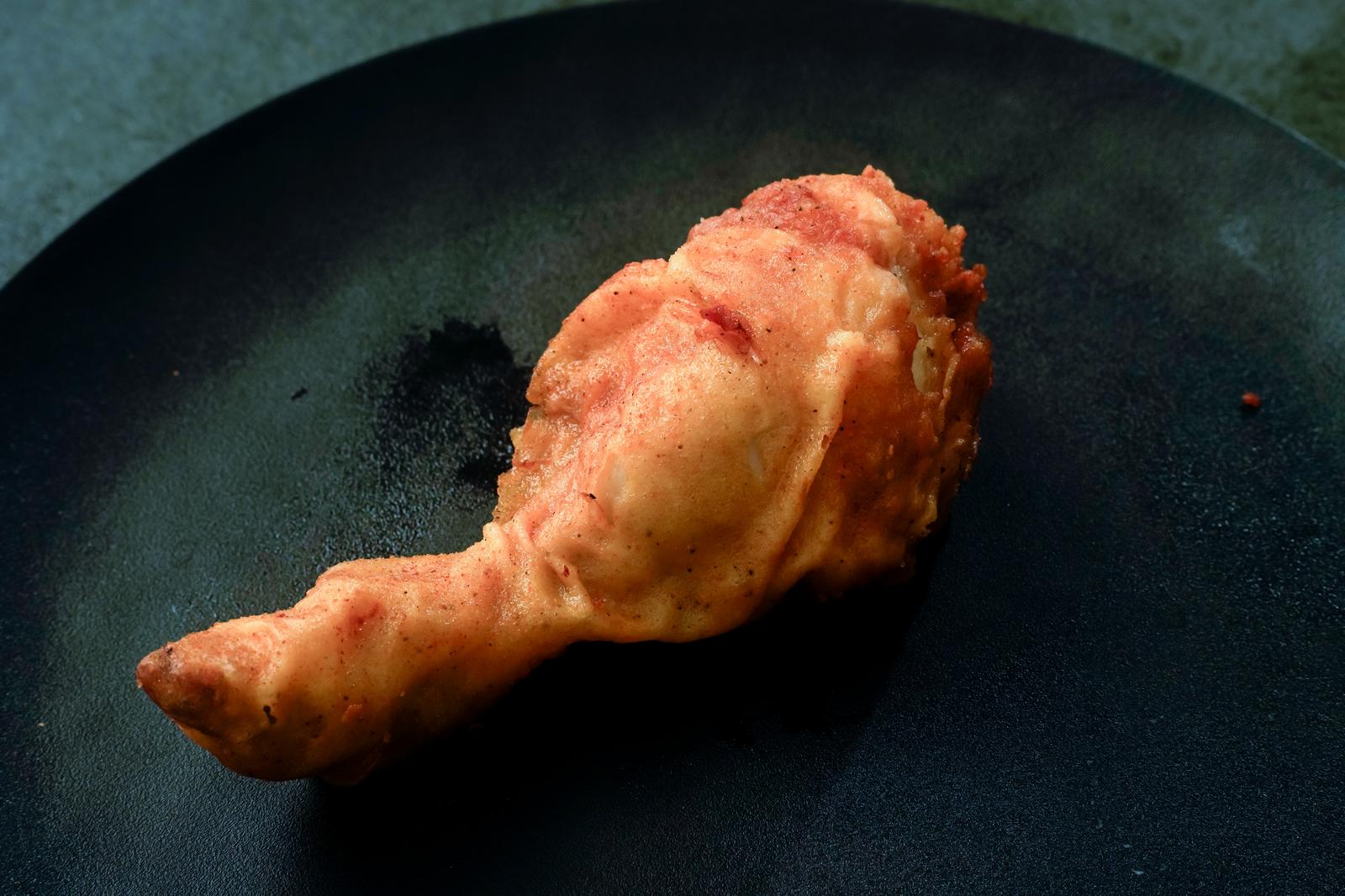 Golden-brown fried chicken drumsticks on a black plate