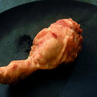 黒い皿に盛られた揚げたてのフライドチキンドラムスティックの写真