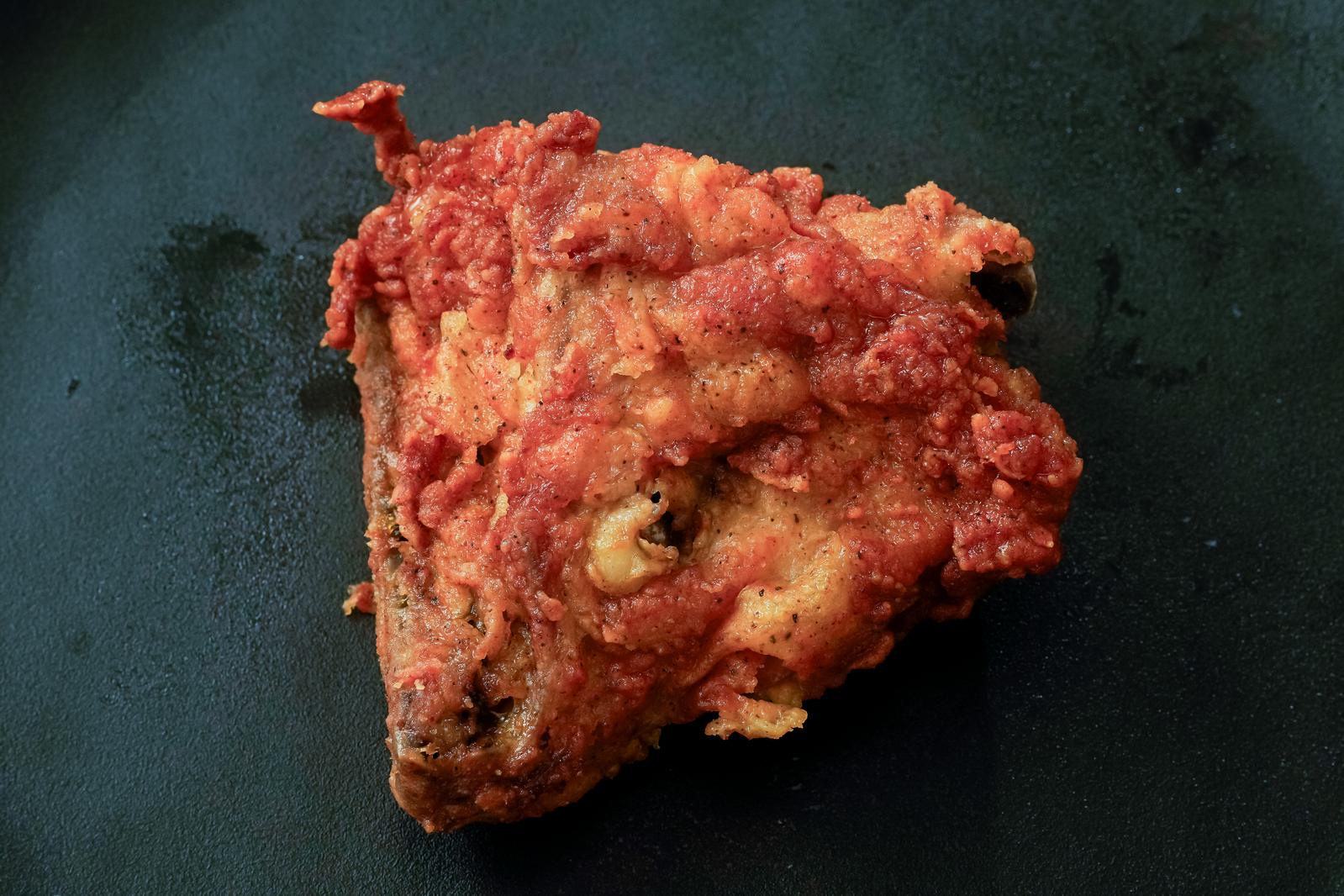 Spicy red breaded fried chicken pieces on a black plate