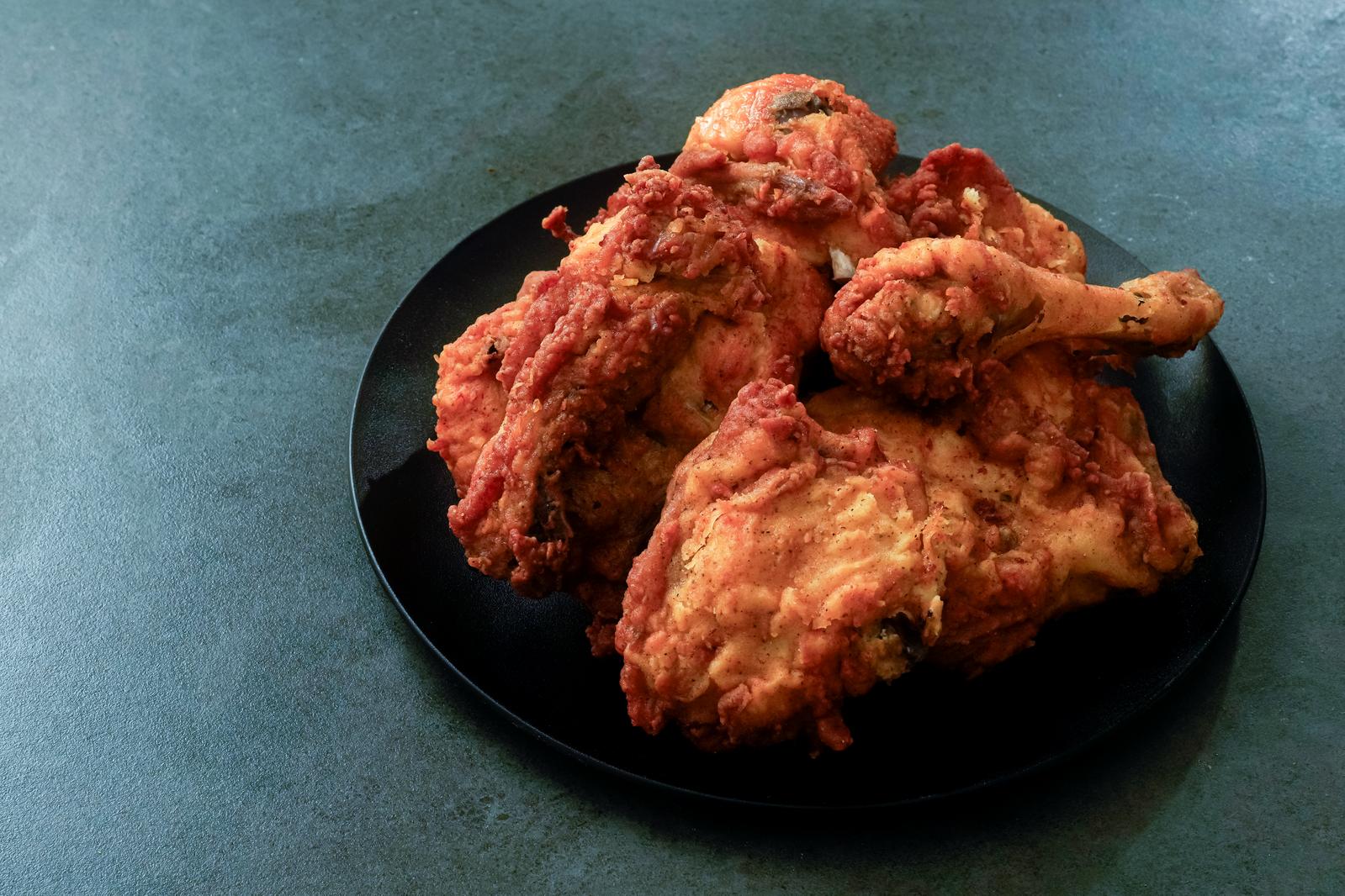 Five bone-in fried chicken pieces on a black plate