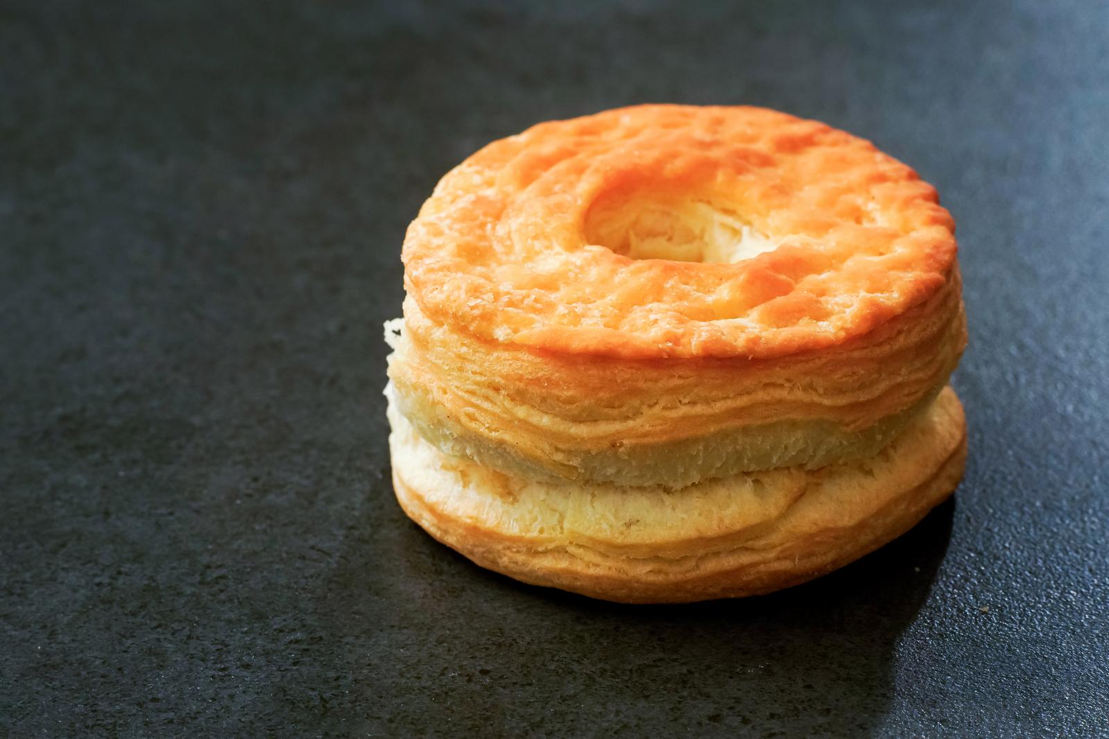 Golden puff pastry biscuits placed on a black table. Donut-shaped baked goods with a hole in the center and crispy layered texture