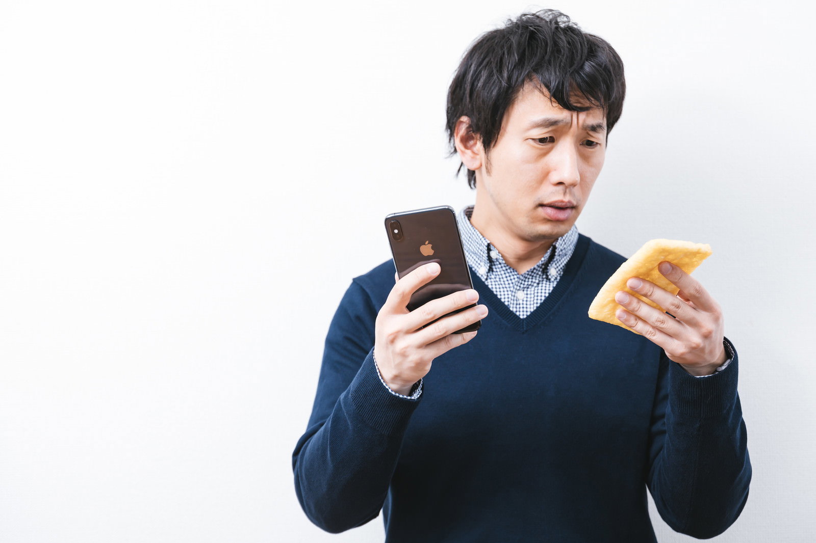 スマートフォンと油揚げを持ち見比べる男性［モデル：大川竜弥］