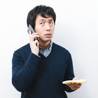 油揚げを手に持ちながら通話する男性の写真