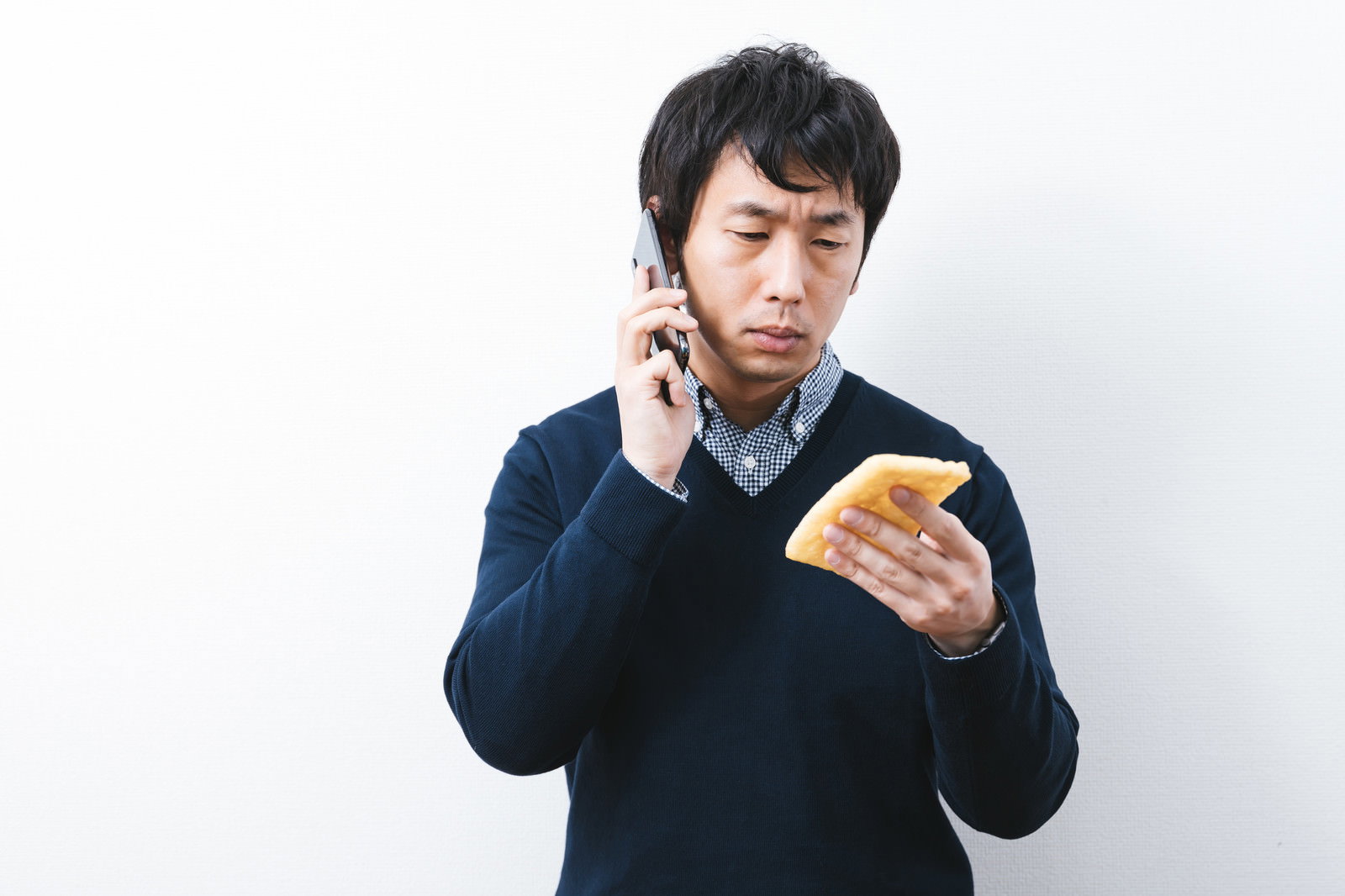 油揚げに書かれたメモを見ながらスマホで通話する紺色セーターの男性［モデル：大川竜弥］