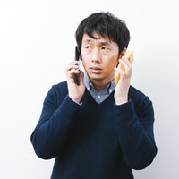 スマホと油揚げの板挟みに遭う男性の写真