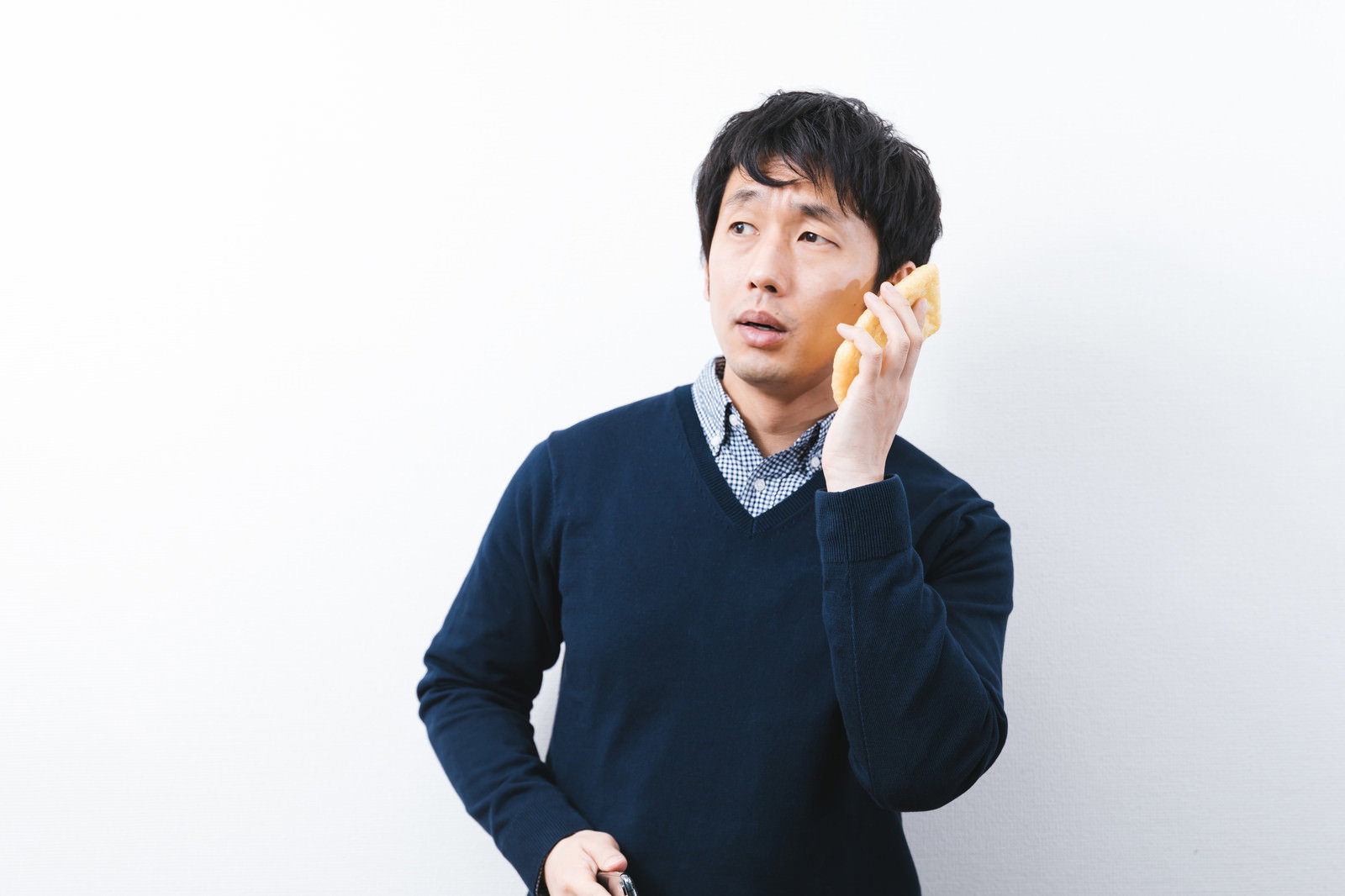 油揚げに耳を当てて音を聞いている紺色セーターの男性［モデル：大川竜弥］