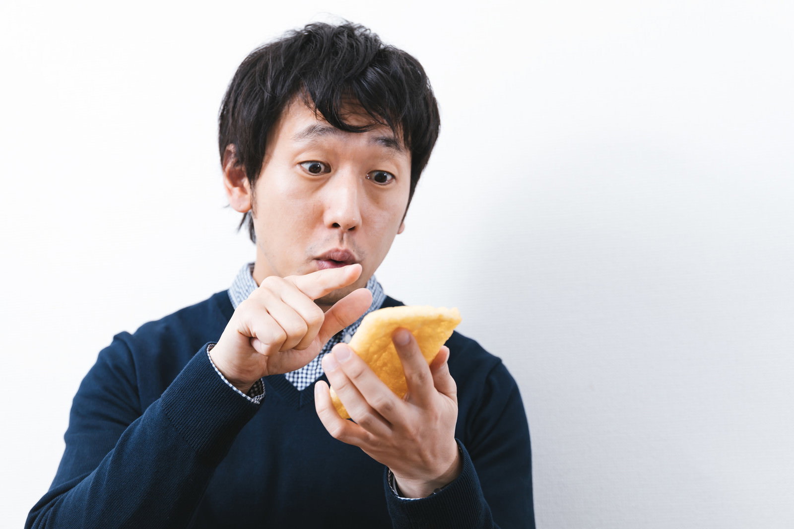 油揚げを持って戸惑う表情の男性、スマホ操作を間違える［モデル：大川竜弥］