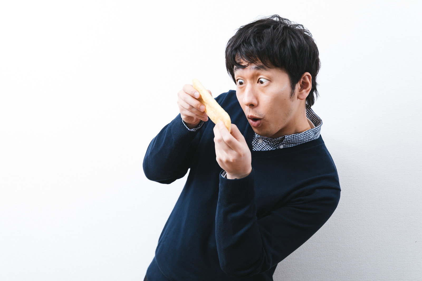 油揚げを持って驚いた表情を見せる黒いニット服の男性［モデル：大川竜弥］