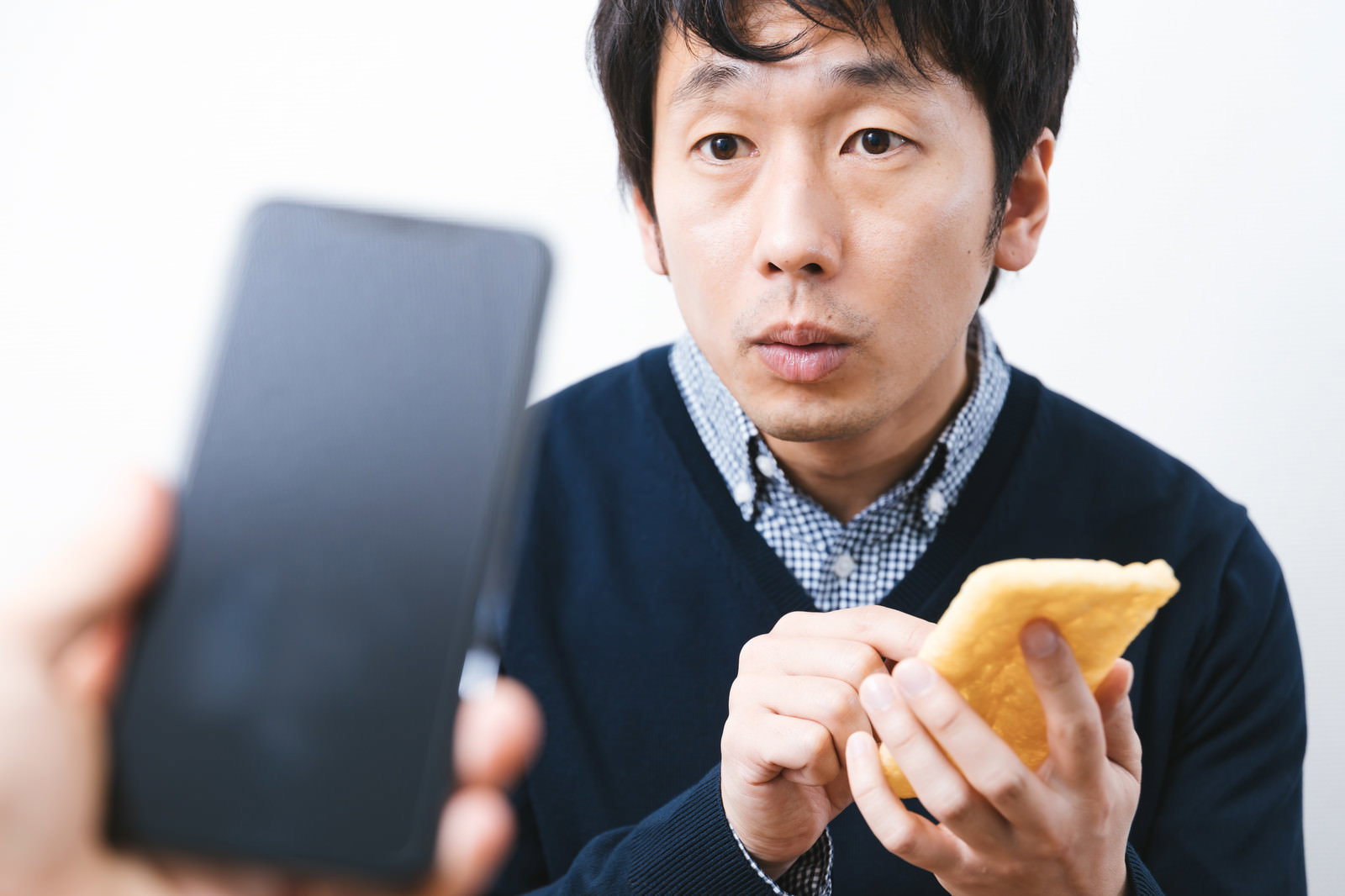 油揚げを持ちスマートフォンを見つめる男性［モデル：大川竜弥］