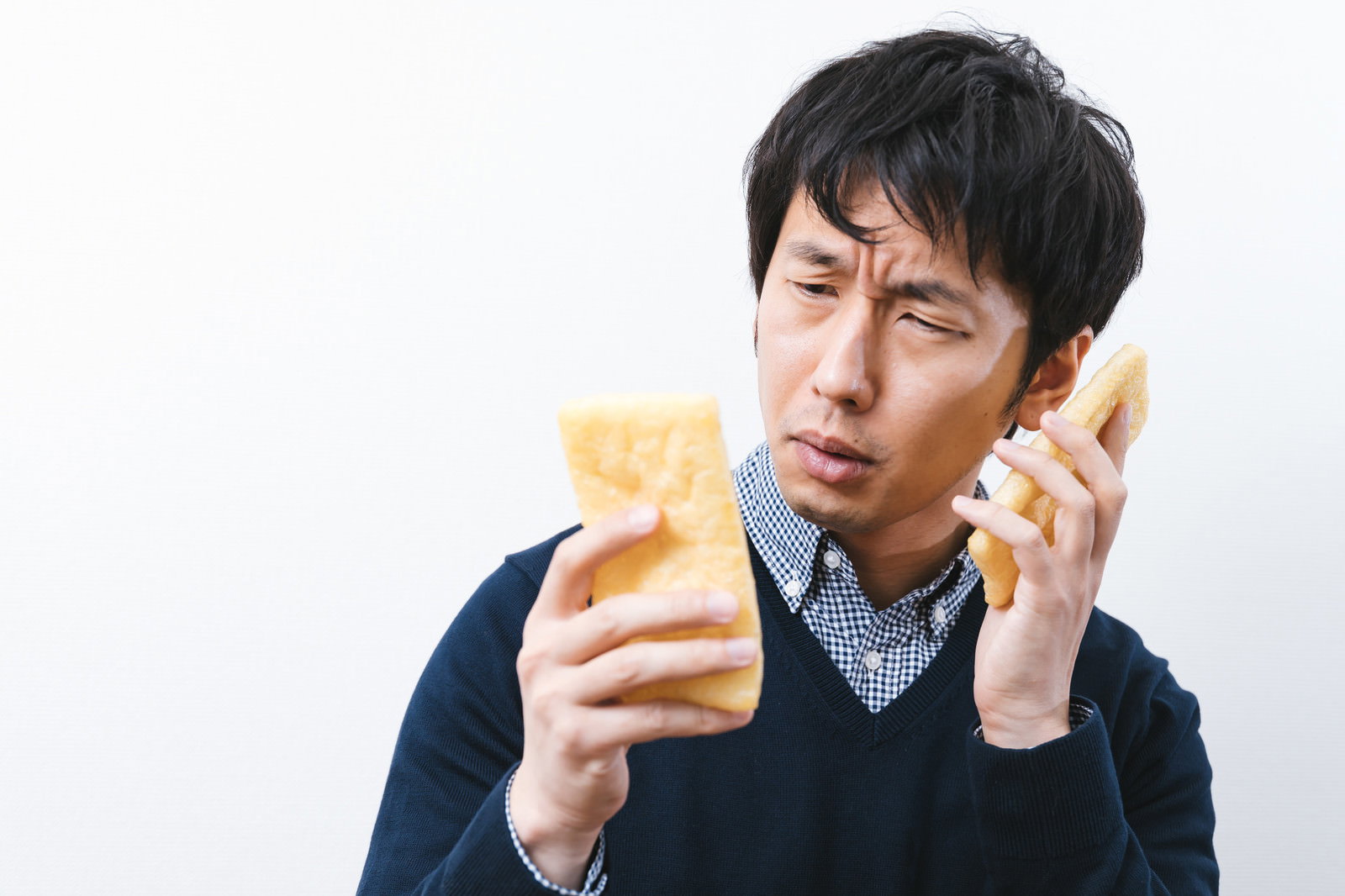 私用スマホと社用スマホを油揚げと間違えて困惑する男性エンジニア［モデル：大川竜弥］