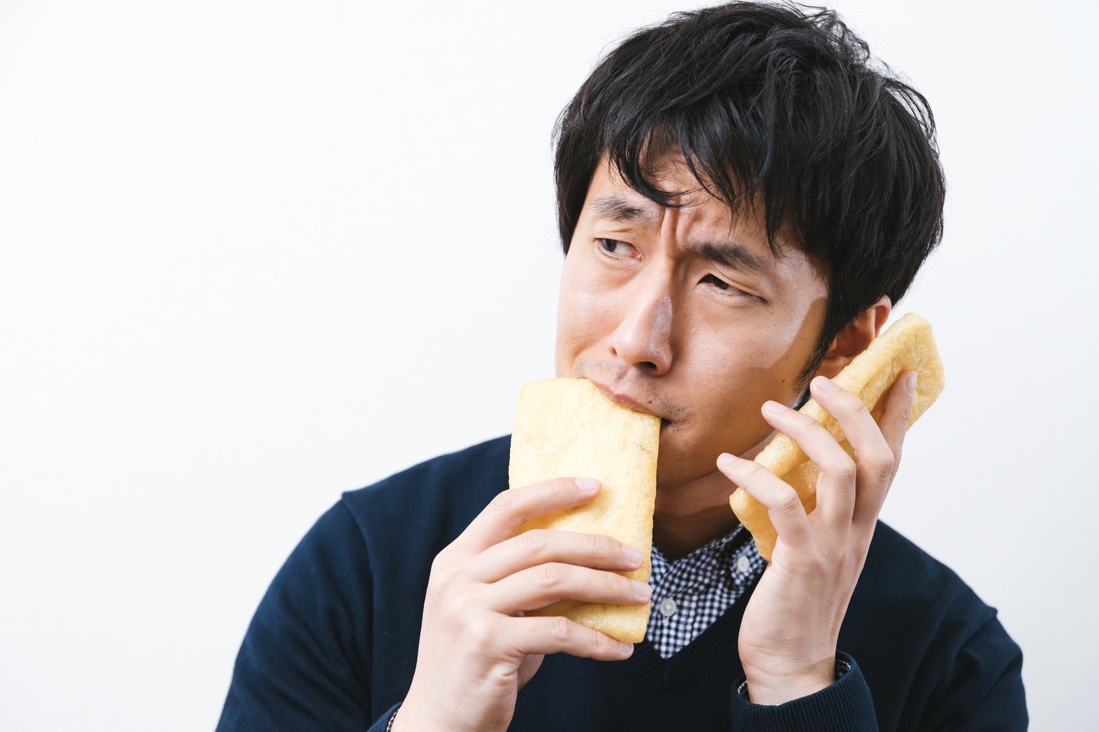 油揚げを手に持って味見をする黒い服の男性［モデル：大川竜弥］
