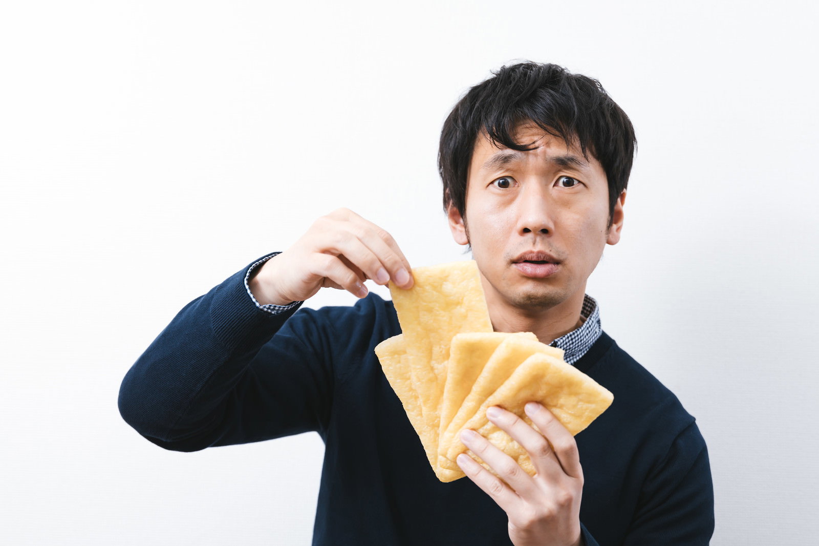 油揚げを手に持ちながらトランプのババ抜きをしている男性［モデル：大川竜弥］