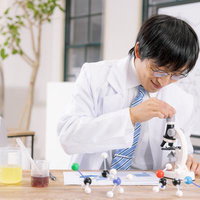おもちゃの顕微鏡で観察実験をする白衣の男性研究者の写真