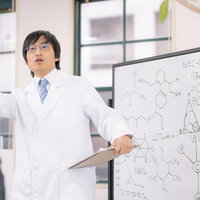 ホワイトボードに化学式を書きながら熱心に講義する科学者の男性の写真