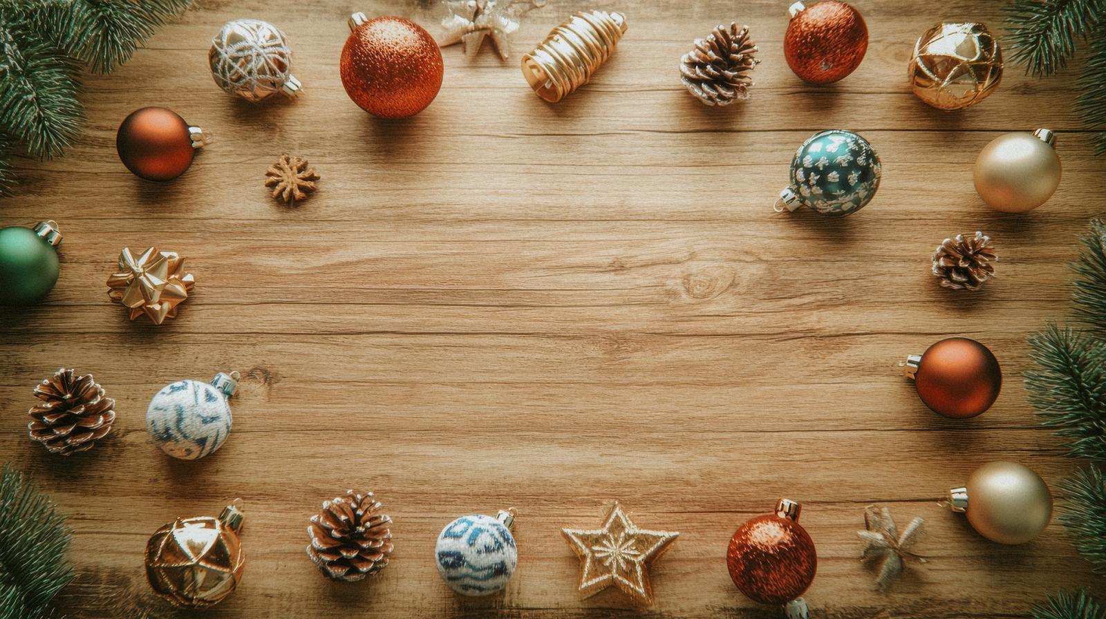 木製テーブルの上にクリスマスオーナメント、松ぼっくり、星飾りが散らばっている俯瞰撮影
