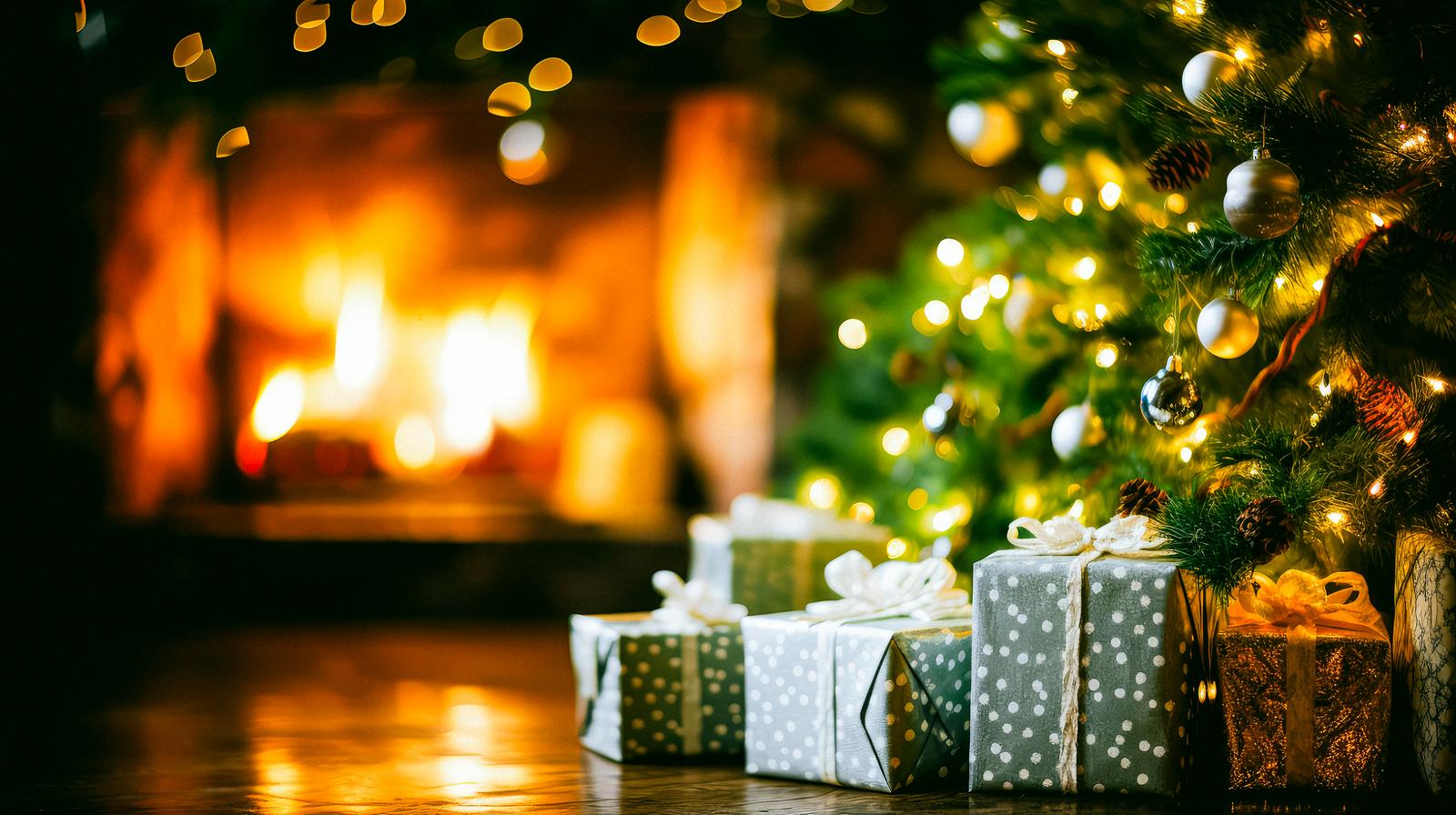 クリスマスツリーの前に積み重ねられたプレゼント箱と暖炉の灯り