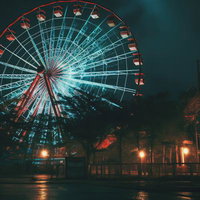 夜間に赤く発光する観覧車とお化け屋敷のホラースリルの写真