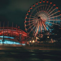 夜間にライトアップされた赤色の不気味な観覧車と遊園地の写真