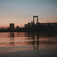 夕焼けに染まるお台場のレインボーブリッジと水面の反射の写真