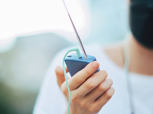 青空の下で携帯ラジオを聴く人のポートレート