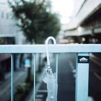 歩道橋の手すりに置き忘れられた白い傘と都市風景の写真