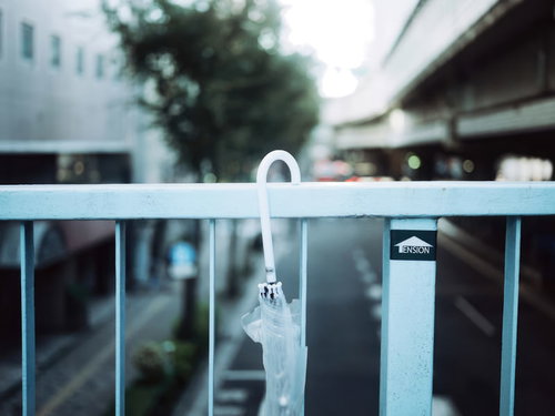 歩道橋の手すりに置き忘れられた白い傘と都市風景