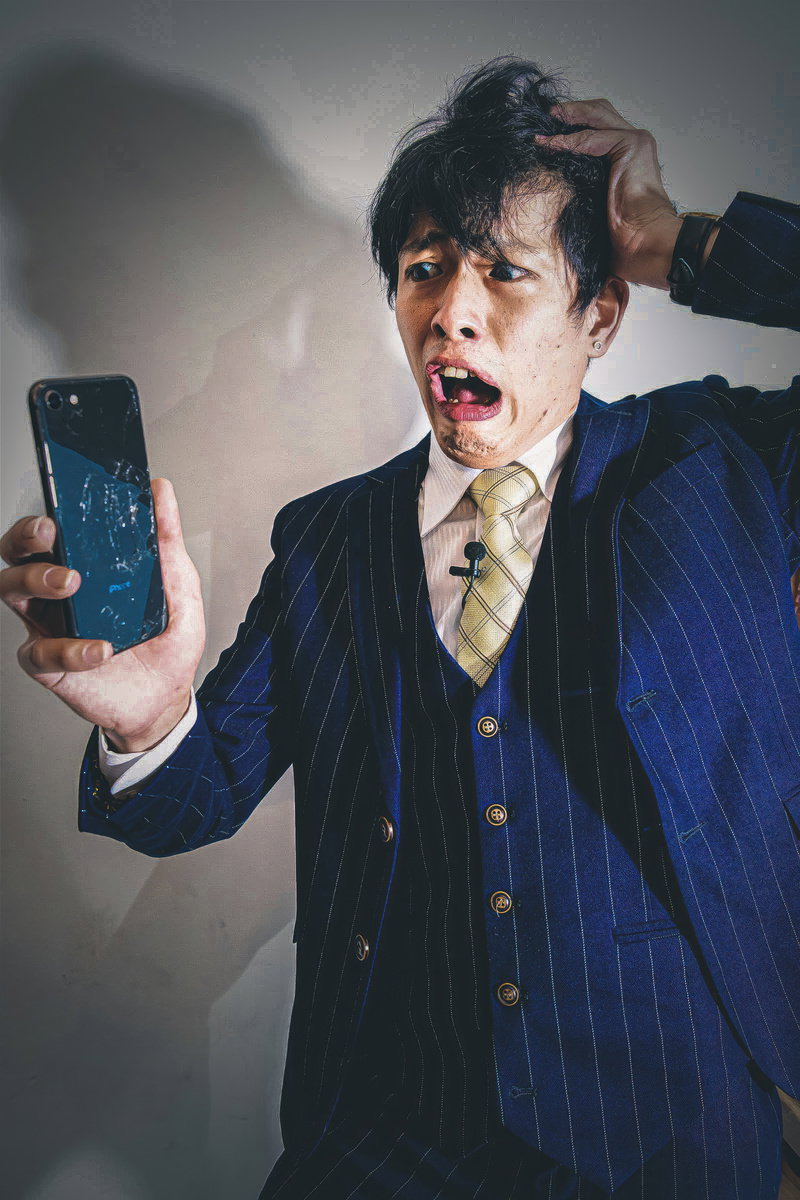 画面にヒビが入ったスマートフォンを持ち頭を抱えて困っている男性［モデル：モデルリリース］