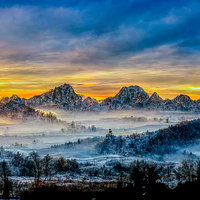 雪国の山々にオレンジ色の日が昇る朝焼けの情景の写真